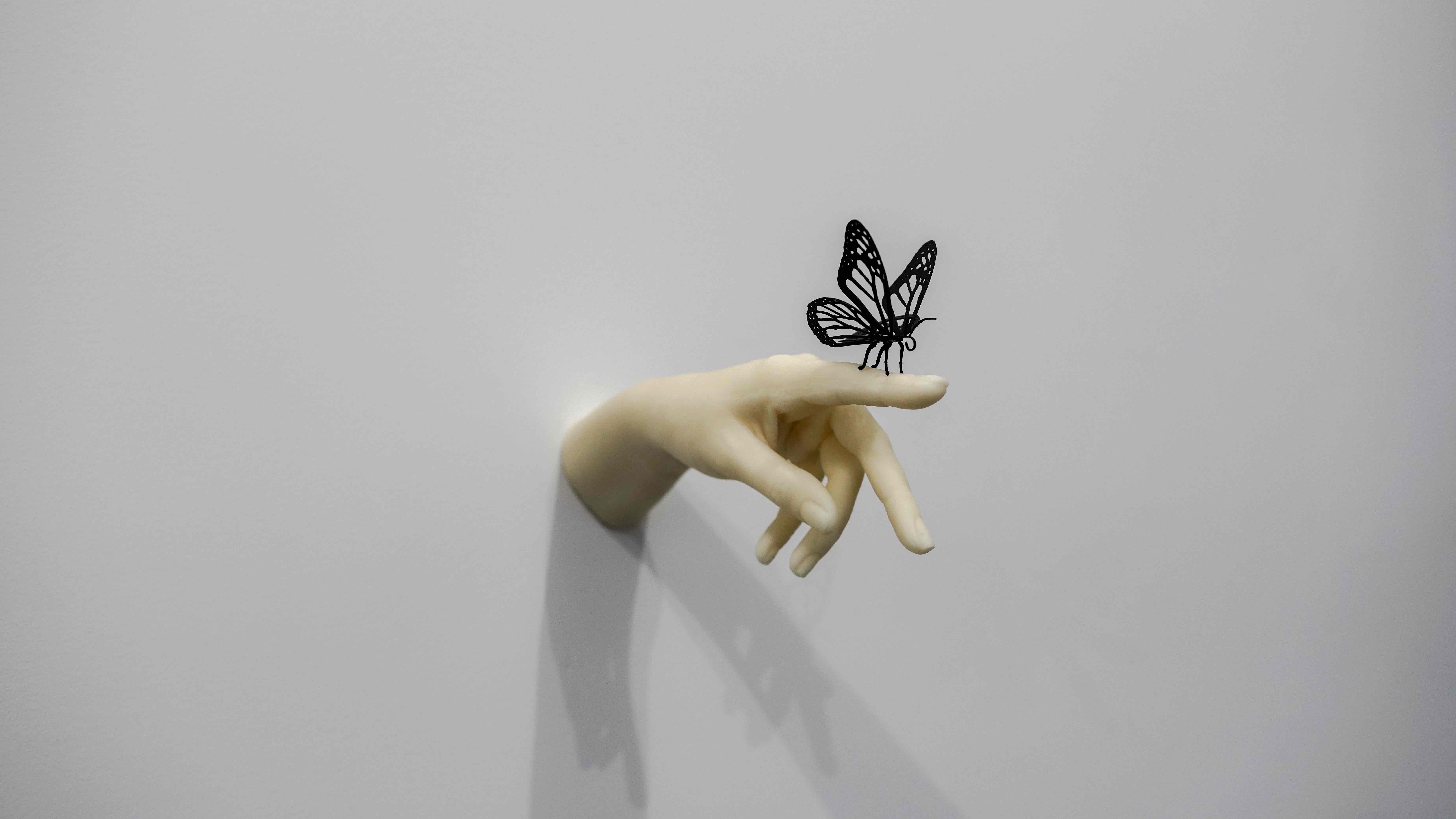 sculpture of a white hand and a black butterfly coming out of a wall