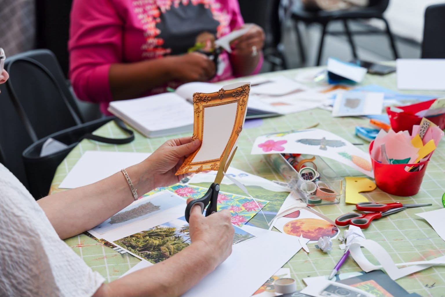 view of people sitting around a table doing paper a craft activity, only their arms, hands, and upper torso are visible