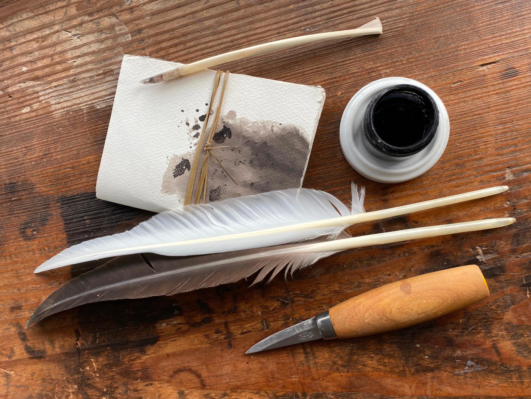 a short knife, feather quills, an ink pot, and a paper stack wrapped in twin sitting on a wooden table