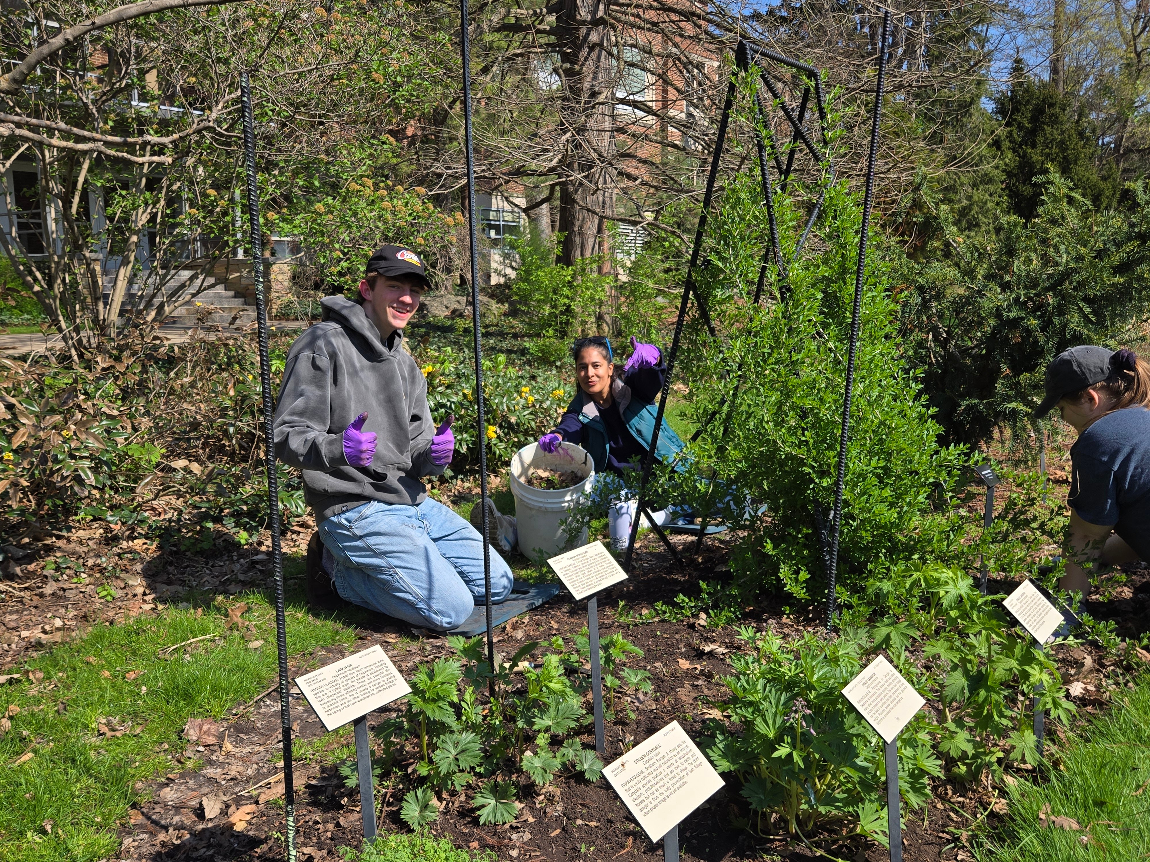 a man and a woman dressed in jeans and long sleeved shirts kneeling in a garden posing with thumbs up signs for the camera