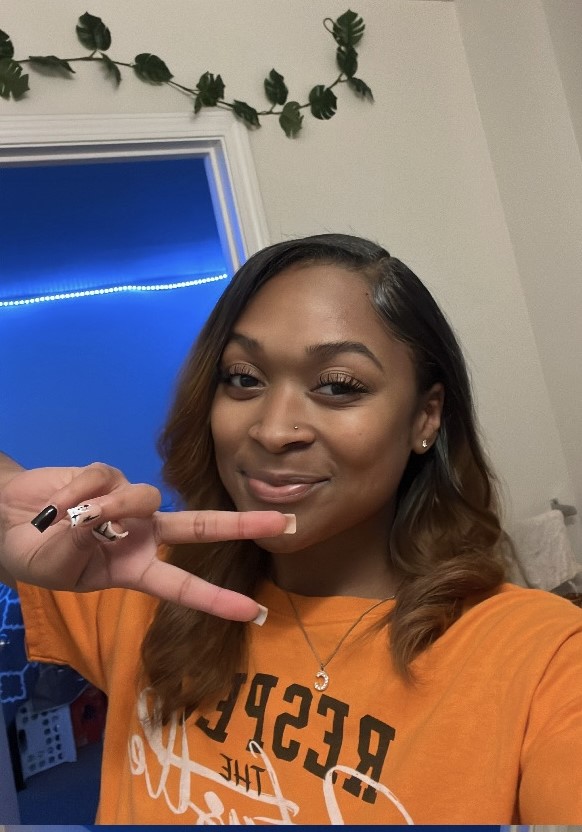 photo of young woman in orange shirt holding up a peace sign