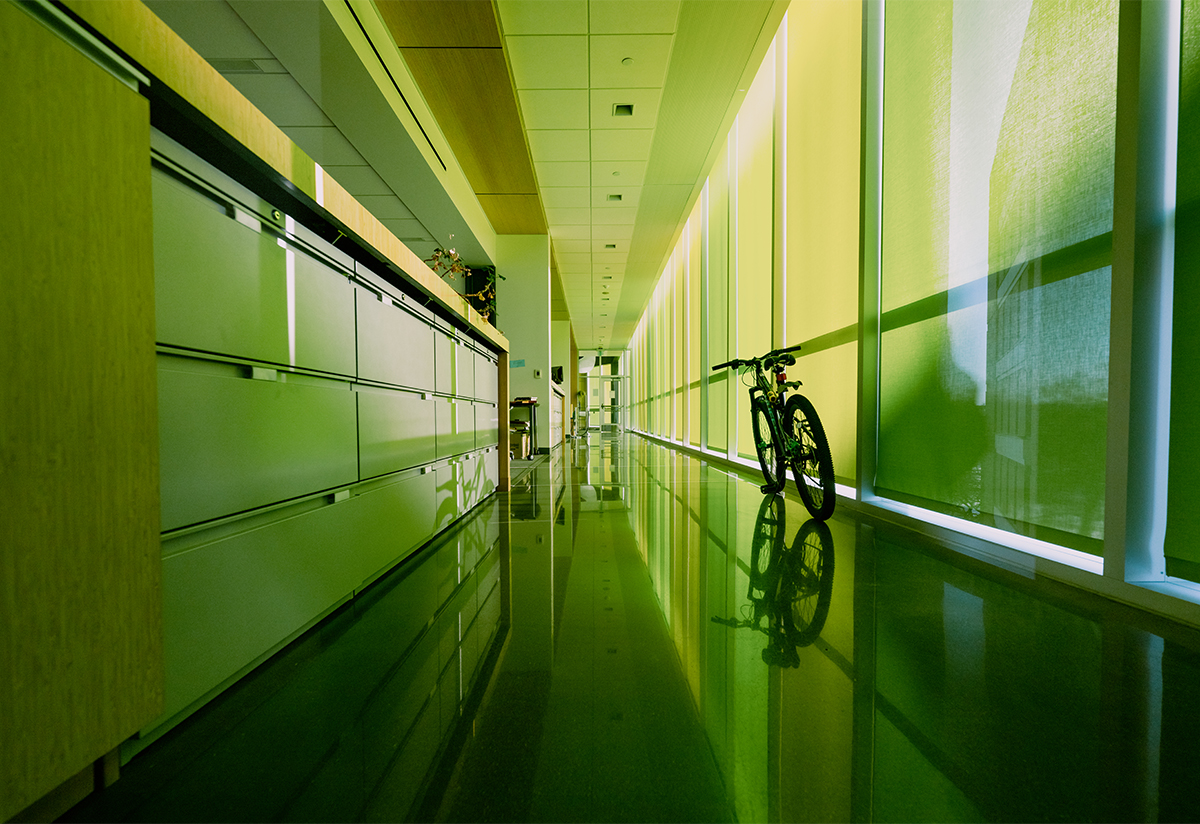 A lone bike rests standing in a long hallway with windows 