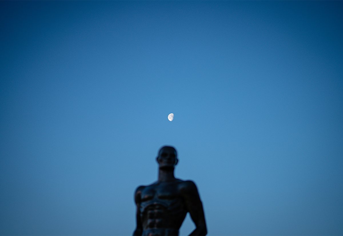 Spartan statue in silhouetted against the blue sky with a crescent moon floating directly overhead