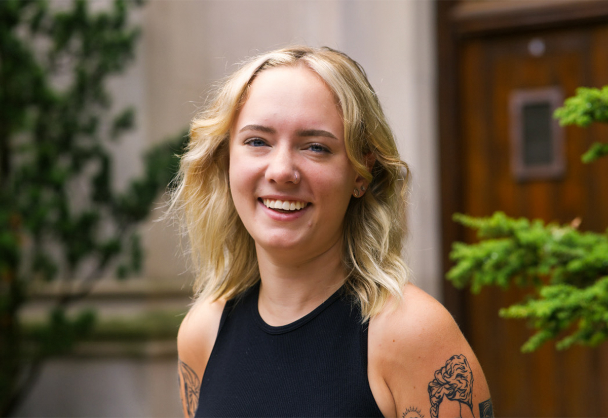 a young blonde student smiling wearing a black shirt and tattoos
