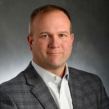 Carmen Crist profile photo, shown wearing a white shirt and grey plaid sportscoat