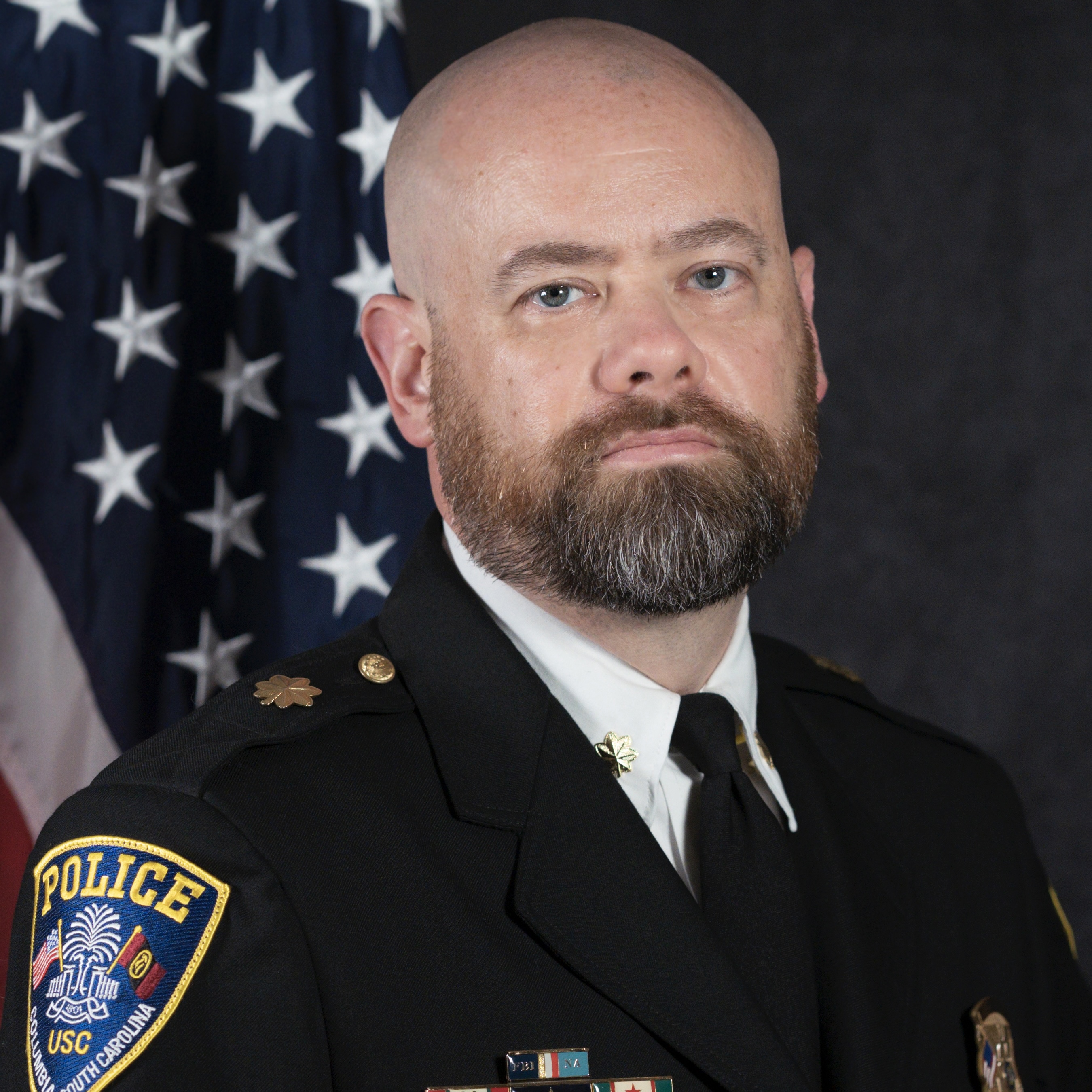 Headshot of T.J. Geary in front of a professional background and an American Flag.