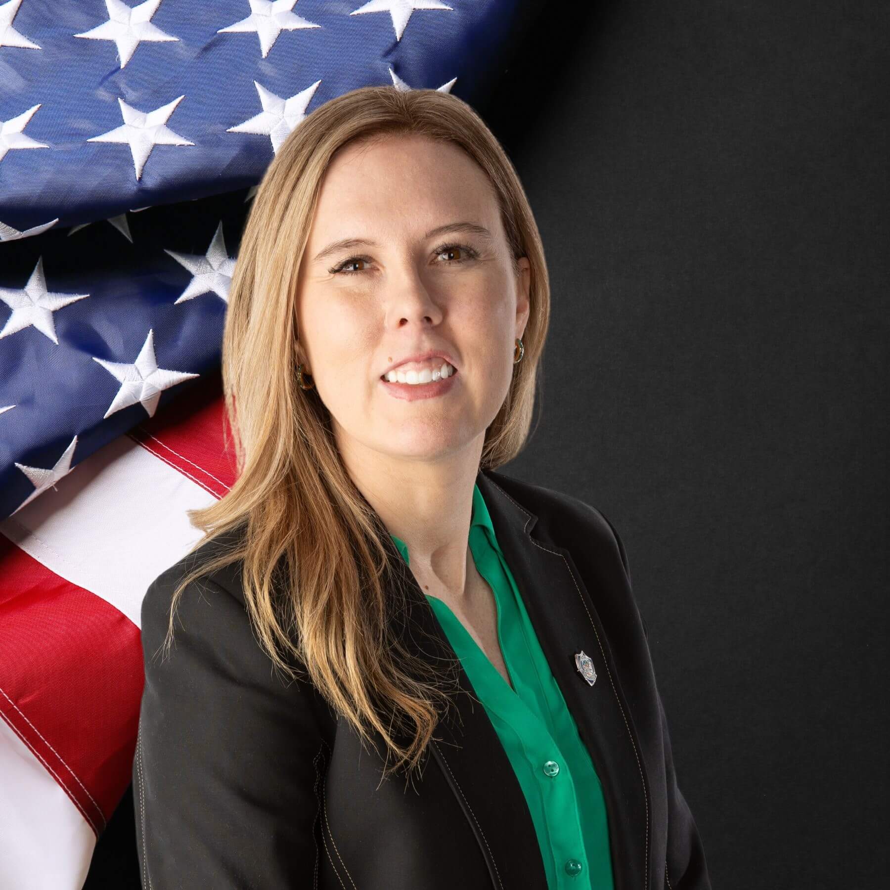 A professional photo of Tara Hall standing in front of an American Flag while wearing a blazer and a green shirt