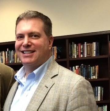 Headshot of Jon Shane in front of bookshelves.