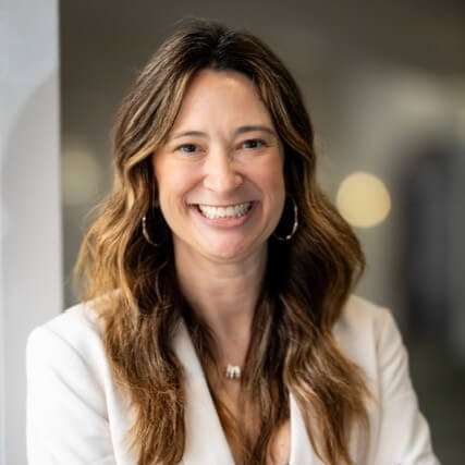 Professional photo of Jessica Toliver in a white blazer standing in front of an open office background