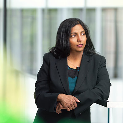 Anjana Susarla, looking off in the distance, wearing a dark jacket and dark shirt, standing outside of a building. 