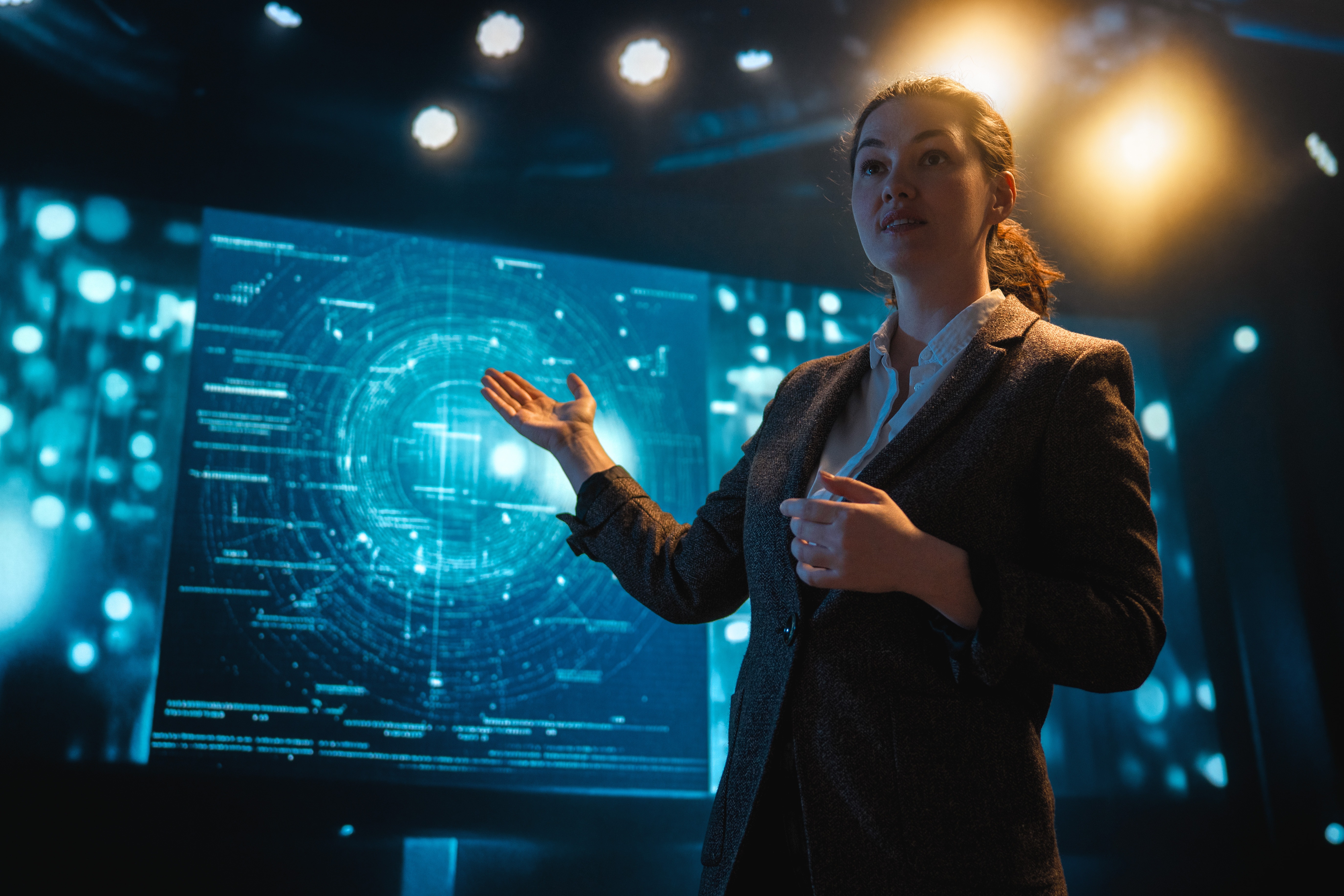 A woman standing in front of a set of screens with various data points on them.