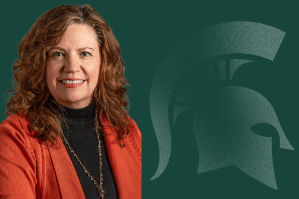 Jennie Schaeffer smiling, wearing a red jacket over a black blouse in front of a green background with a Spartan helmet logo.