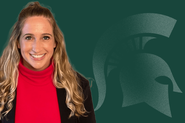 Juli Fusi smiling, wearing a black jacket over a red sweater in front of a green background with a Spartan helmet logo.