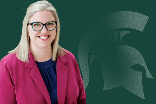Kara Yermak smiling, wearing a pink jacket over a dark blouse in front of a green background with a Spartan helmet logo.