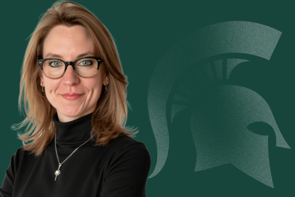 Headshot of Kate Birdsall, director for Faculty and Academic Staff Affairs, from the shoulders up with a closed-mouth smile and wearing black in front of a green background featuring a Spartan helmet logo.