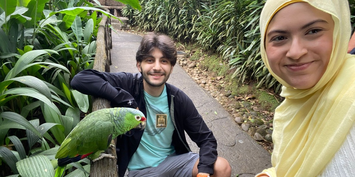 Two students taking a selfie with a green parrot