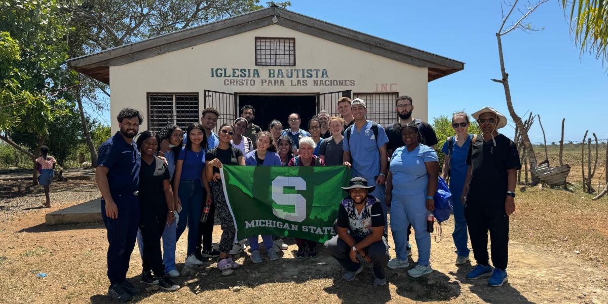 MSU medical students and faculty holding a Michigan State flag in front of a church in the Dominican Republic