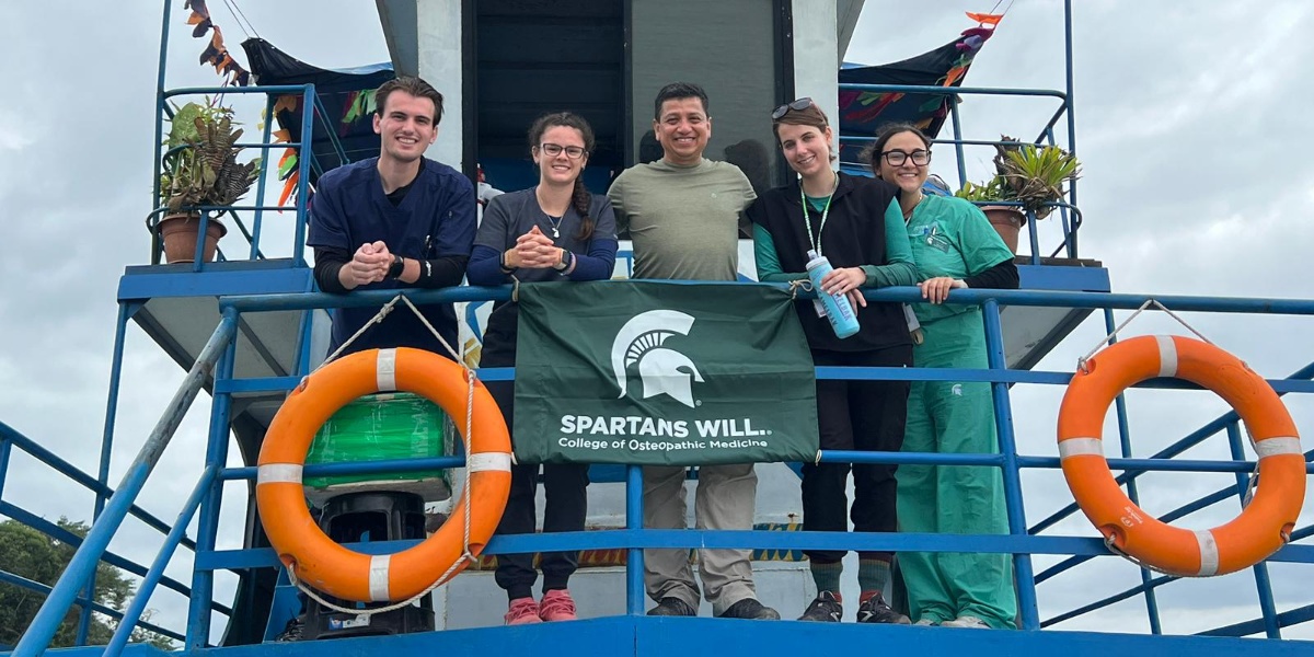 MSU College of Osteopathic Medicine students and faculty holding a "Spartans Will" MSU flag on the Amazon King medical care boat.