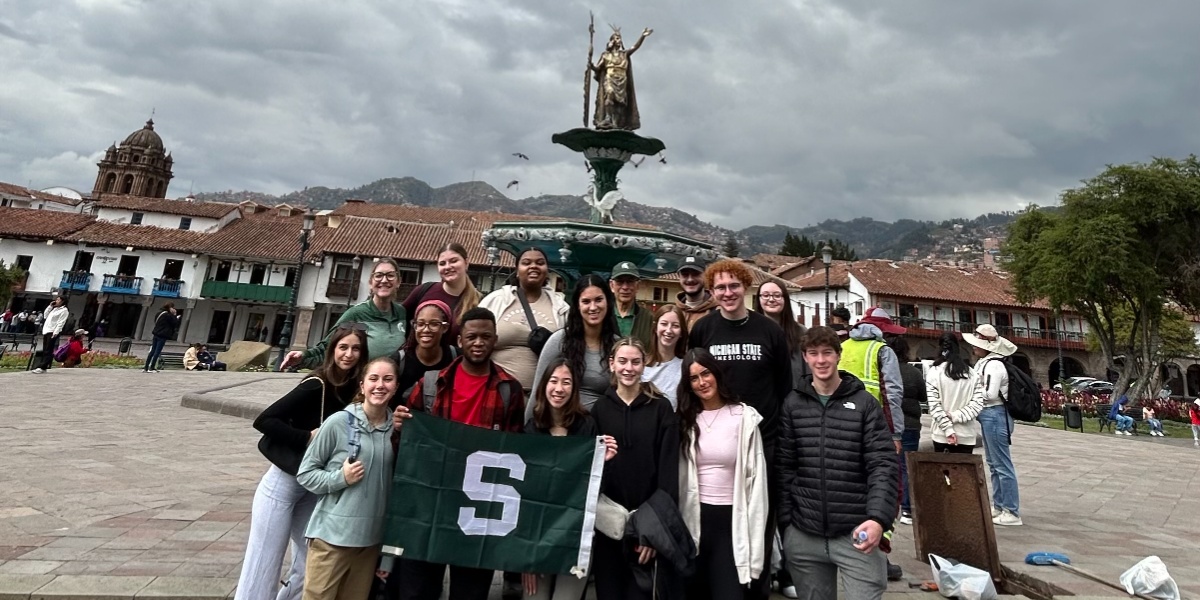 MSU students holding a Michigan State flag at the Inca statue in the Plaza Mayor, Cusco, Peru.