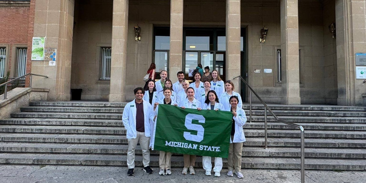 MSU students holding a green Michigan State Flag in front of the Josep Trueta University Hospital in Girona, Spain