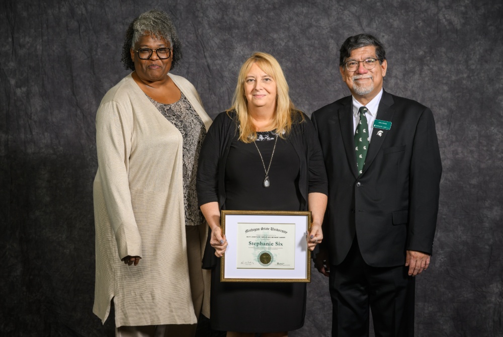 MSU Global Health Studies Assistant Director Stephanie Six holding the 2026 Ruth Jameyson Above and Beyond Award. She is joined by colleagues Wendi Winston and John Garcia
