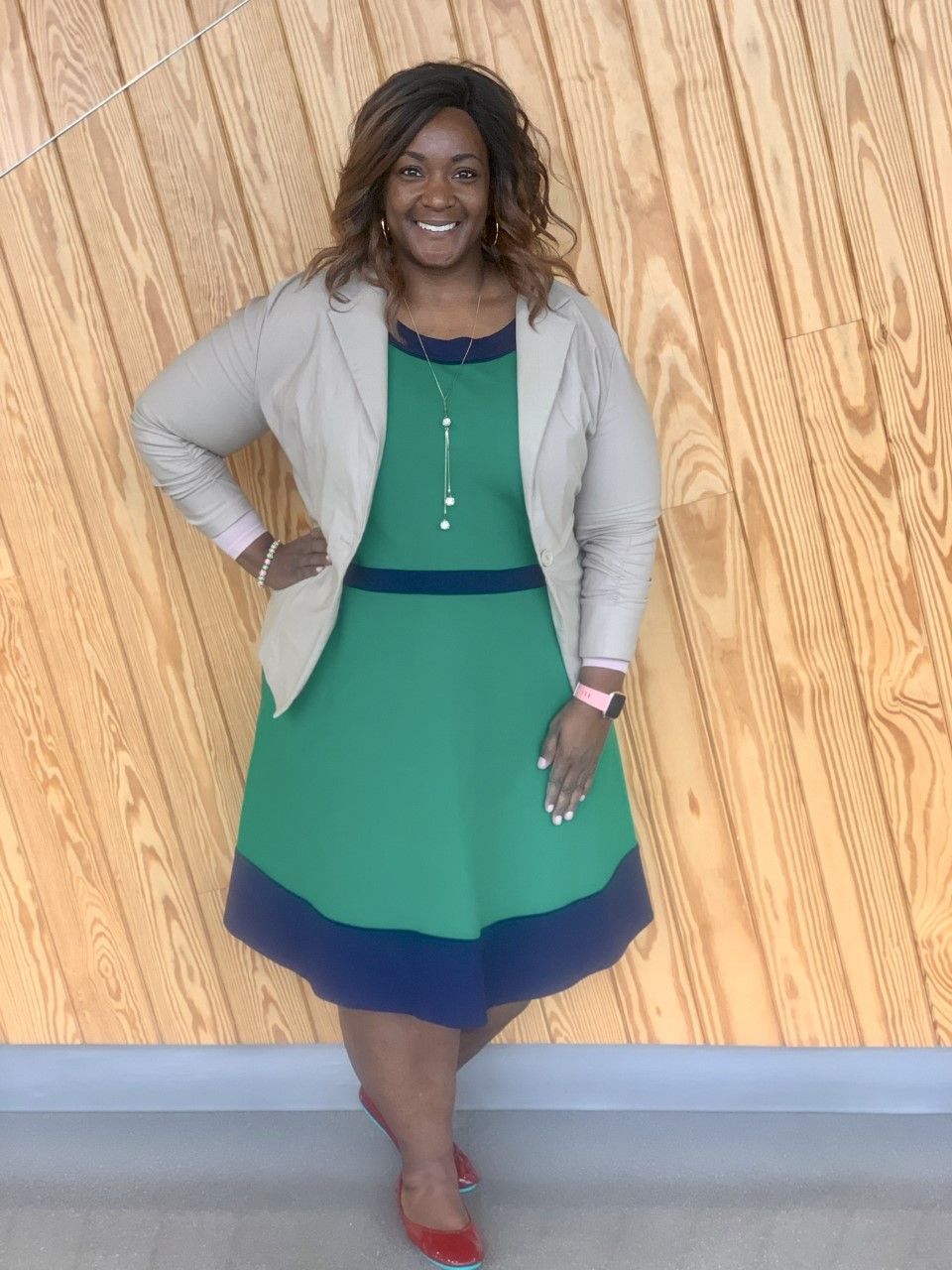 Dee Jordan in a green and blue dress, standing in front of a wooden wall.