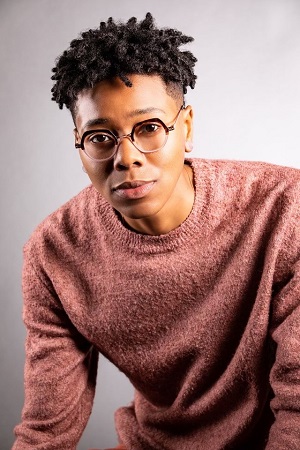 Briona Simone Jones, dressed in an orange sweatshirt in front of a grey background.