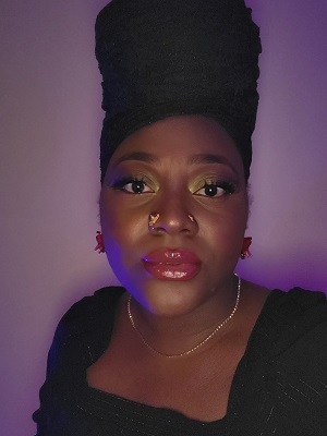 Monique Noel dressed in black, standing in front of a purple backdrop.