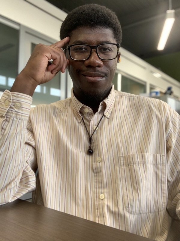 Antonio White in a white striped shirt and black glasses, sitting at a table. His elbow is resting on the table with his hand on the side of his head.