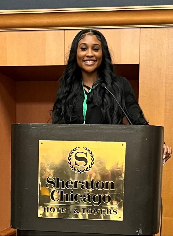 Jada Gannaway speaking into a microphone while standing behind a brown and gold podium that reads, "Sheraton Chicago Hotel & Towers."