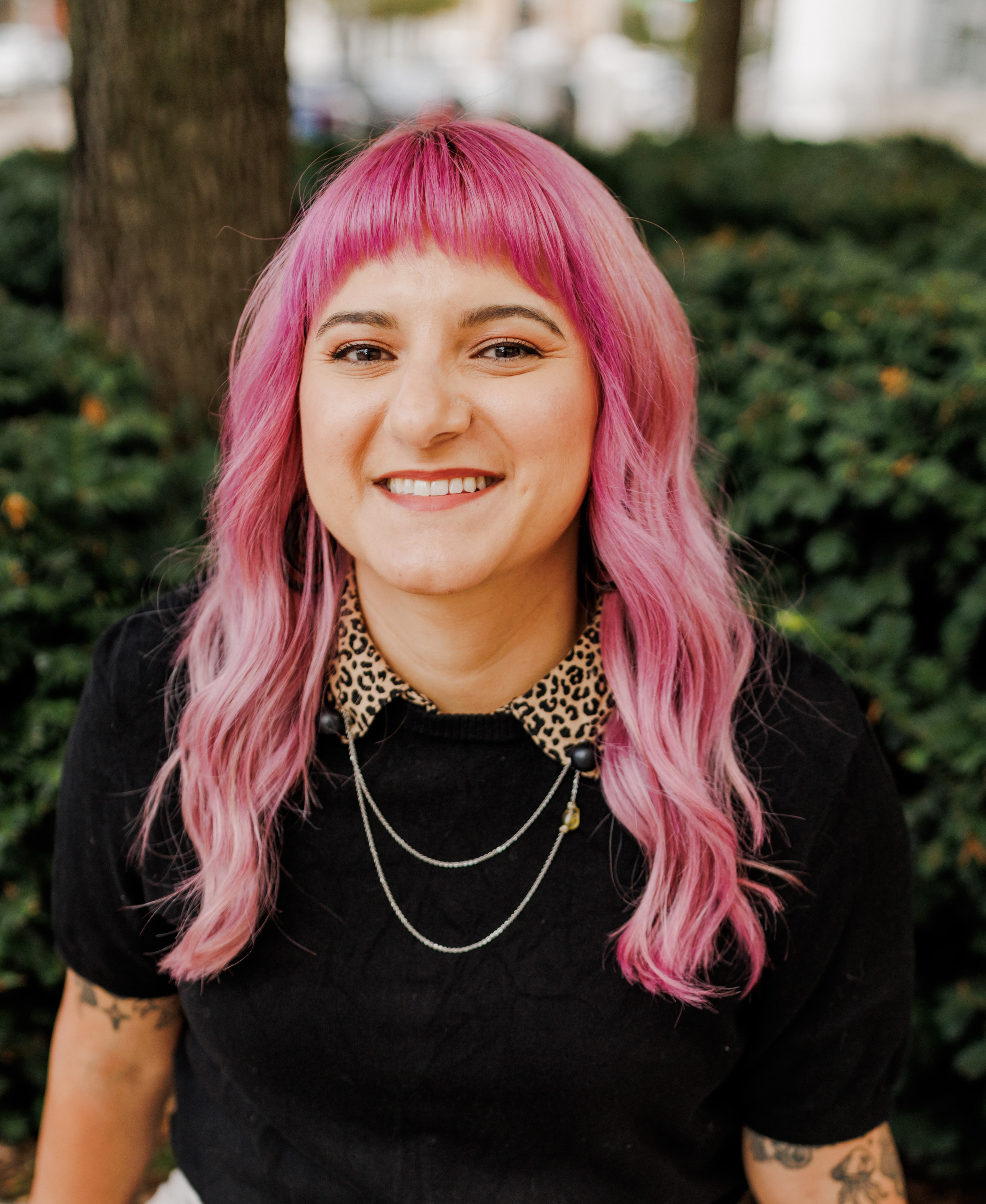 Sabrina sitting outside, wearing a black shirt with leopard print collar. Her hair is dyed pink.