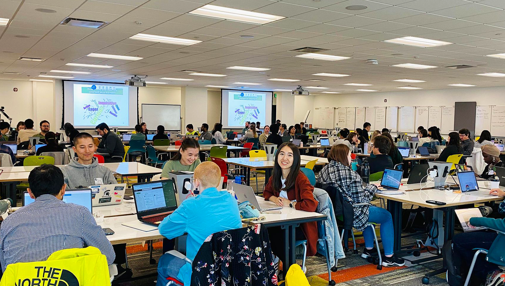 A large group of students are seated around a series of tables in a conference room during the CCT institute.