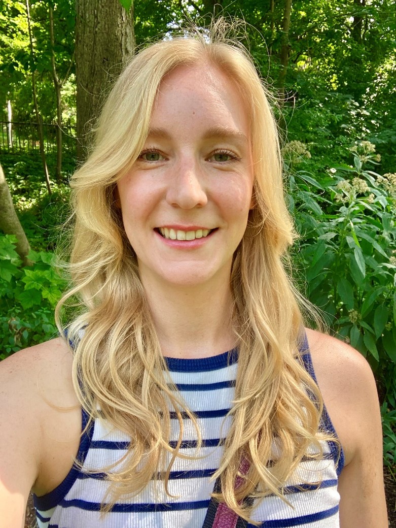 Helena Stech in a white and blue tank top, standing outdoors.