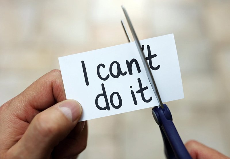 A hand is holding an index card that reads "I can't do it." Another hand is cutting the card so the "can't" now says "can."