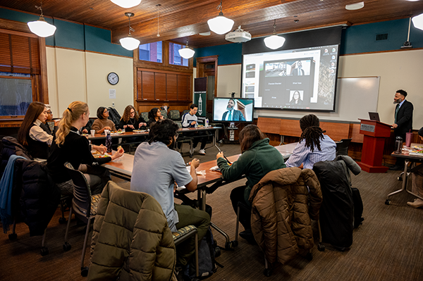A group of students is seated around a U-shaped table. Dean Pero Dagbovie is standing at a podium and speaking.