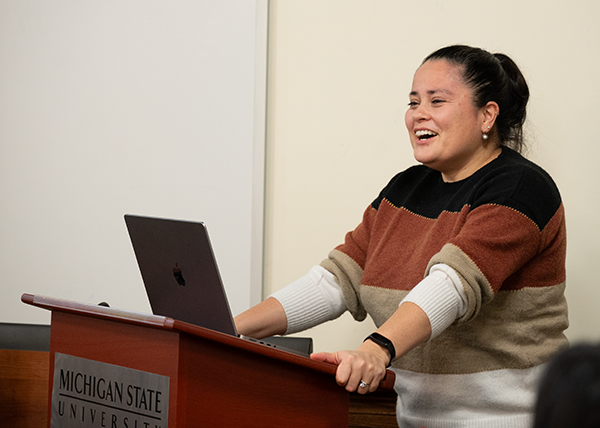 Meg Moore stands behind a podium and speaks.
