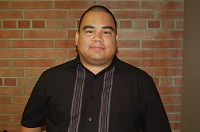 Antonio in a black shirt, standing in front of a brick wall.