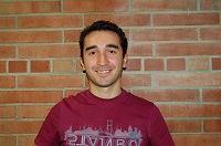 Baburhan in a red shirt, standing in front of a brick wall.