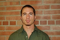David in a green shirt standing in front of a brick wall.