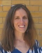 Ann in a blue and white shirt, standing in front of a yellow brick wall.