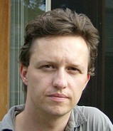 Dominik in a grey shirt, sitting in front of a window.