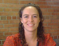 Emily in an orange shirt, standing in front of a red brick wall.