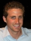 Michael in a white button-up shirt against a black backdrop.