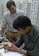 Two men are hunched over table, looking at a document.