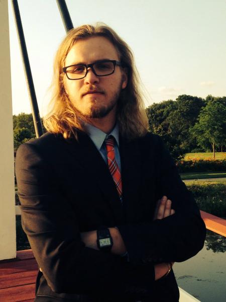 Samuel in a blue shirt and black suit coat, with a red tie.
