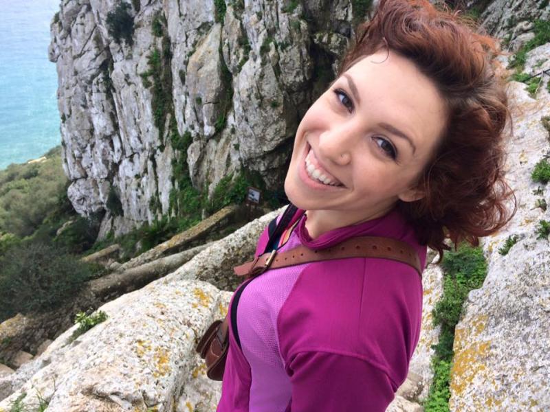 Adrienne standing at the edge of a cliff in a pink shirt.
