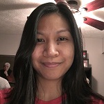 Annabelle in a red shirt, standing in a room in front of a ceiling fan.