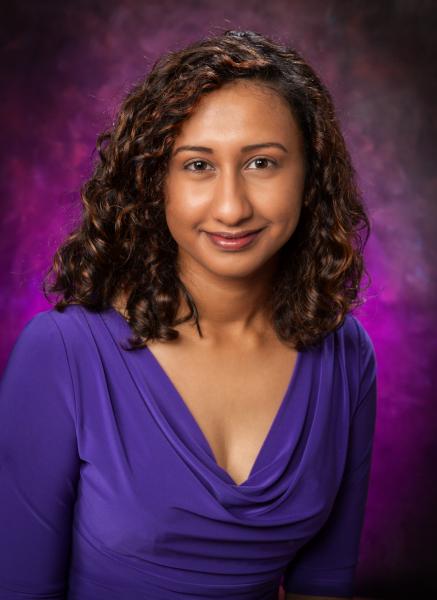 Sudha Sankar wearing a bright purple shirt in front of a purple backdrop.