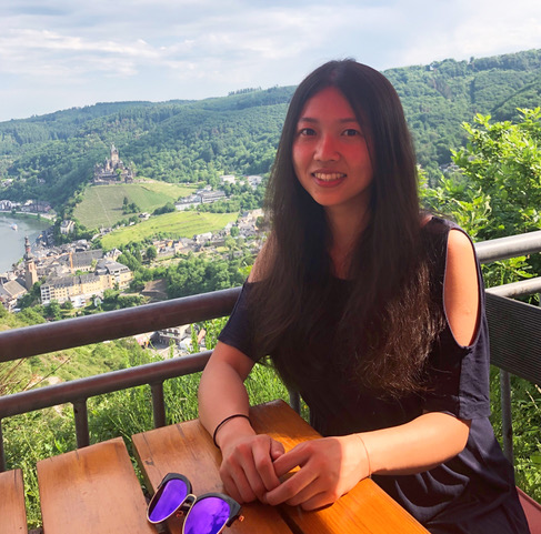 Tianyi Kou in a black shirt, seated at a picnic table overlooking a forested landscape.