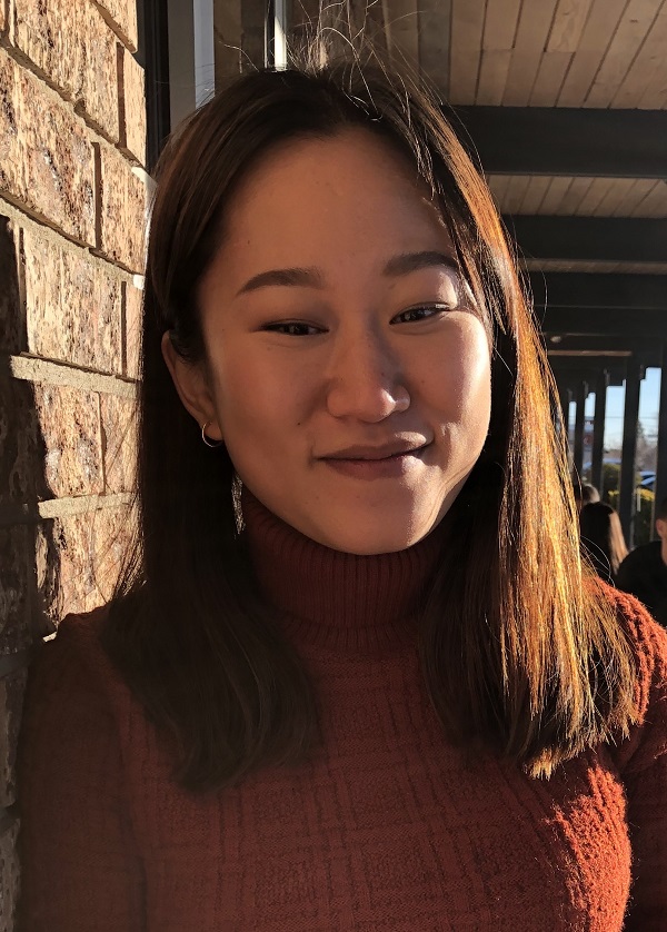 Stephie Minjung Kang in a red sweater standing next to a brick wall.